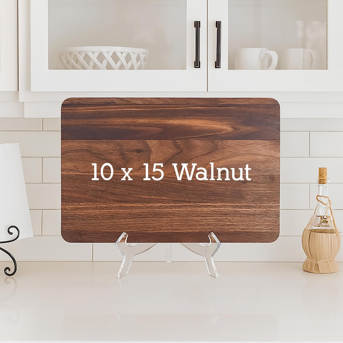 A rectangular walnut cutting board, 10 x 15 inches, with the text "10 x 15 Walnut" in white. The board is displayed on a clear acrylic stand, showcasing its rich wood grain.