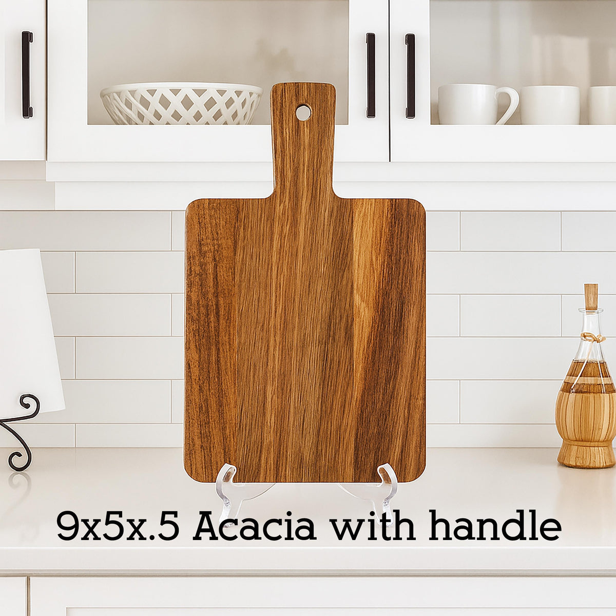 A rectangular acacia wood cutting board with a handle. The board is 9 inches long, 5 inches wide, and 0.5 inches thick. The wood grain is visible. The text "9x5x.5 Acacia with handle" is at the bottom.