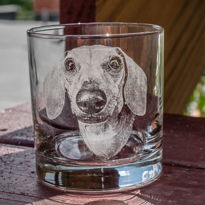 A clear glass tumbler with an etched image of a dachshund dog. The dog is facing forward with its ears perked up and its tongue sticking out.