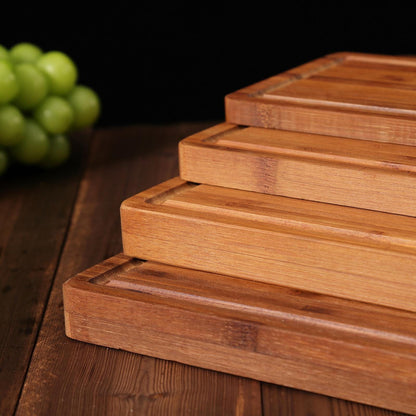 Four wooden cutting boards stacked on top of each other. The boards are made of light brown bamboo and have a rectangular shape. The boards have grooves on the surface to help drain liquids.