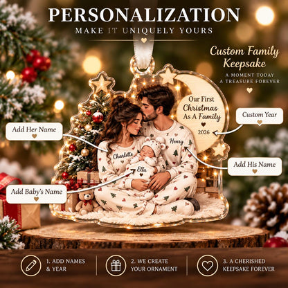 May include: A clear acrylic Christmas ornament featuring a printed illustration of a family of three wearing matching pajamas. The design includes a Christmas tree, a crescent moon with the text Our First Christmas As A Family 2026, and space for custom names.
