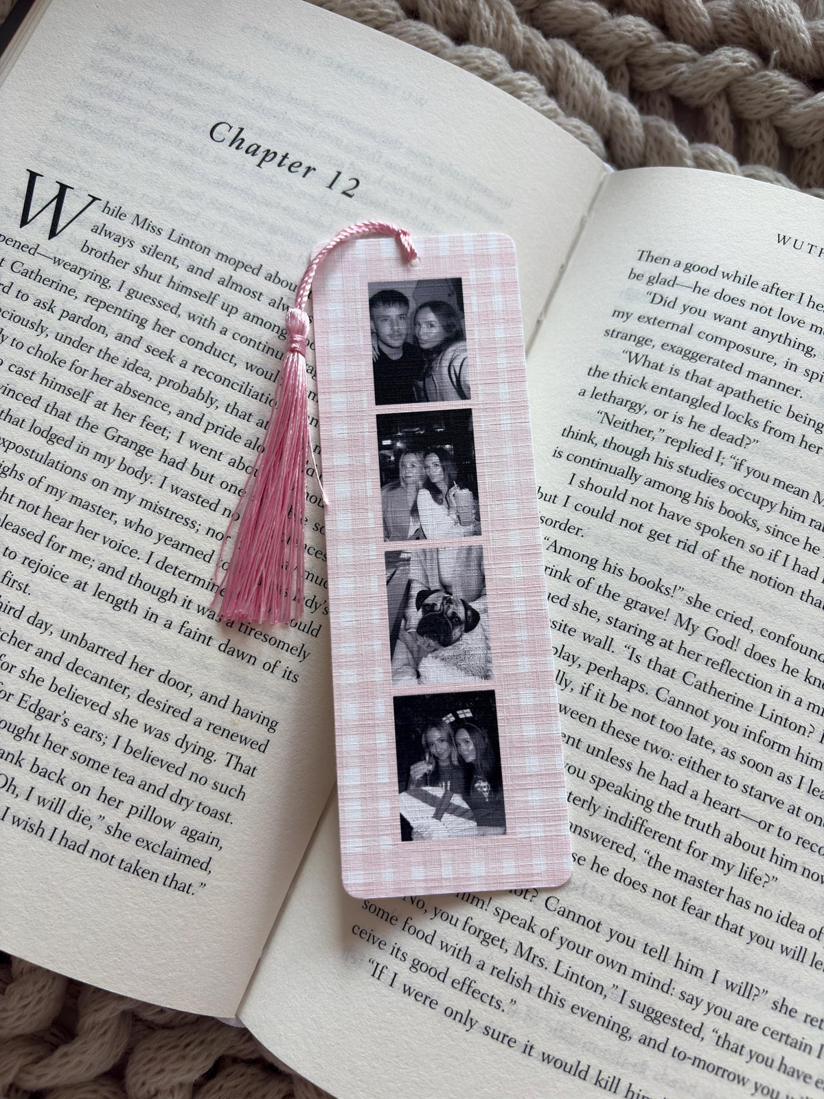 A rectangular bookmark with a light pink and white gingham pattern featuring a vertical strip of four black and white photographs. A light pink tassel is attached to the top center of the bookmark, which is resting on an open book.