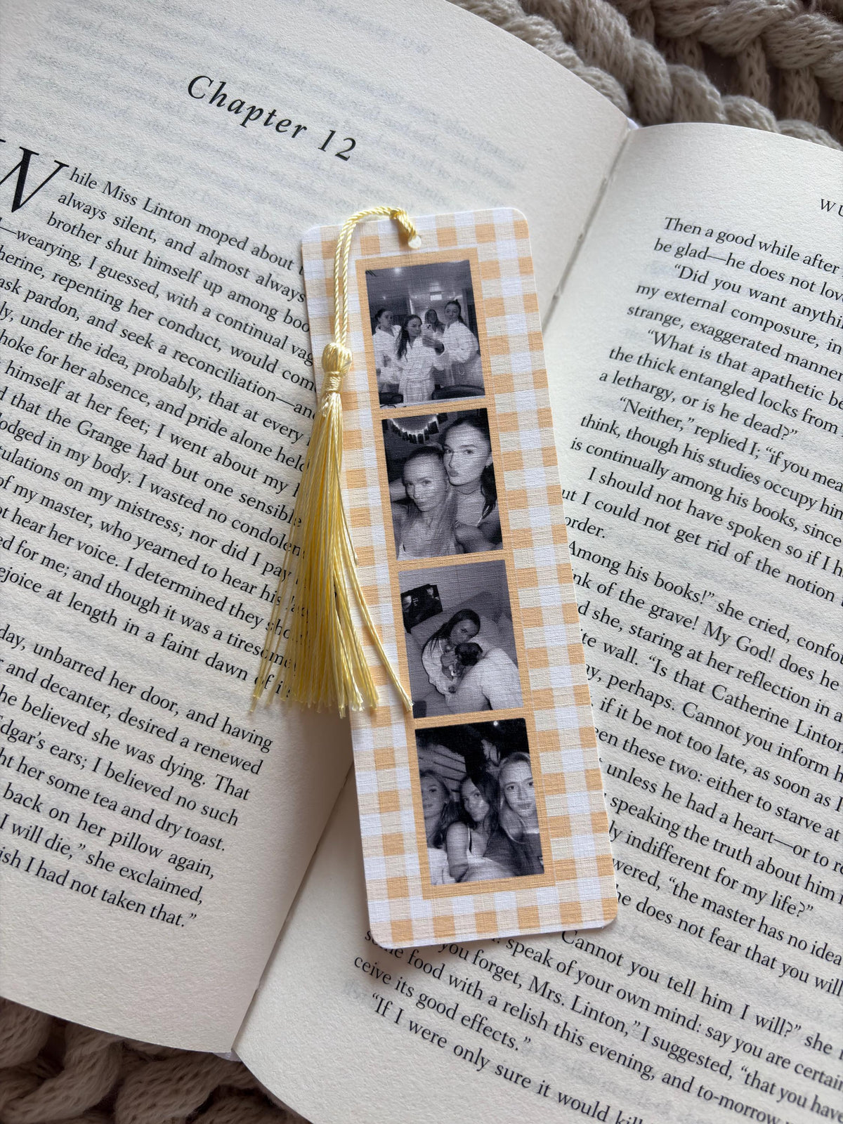 A rectangular bookmark with a light orange and white gingham pattern featuring four vertical black and white photographs of people. A pale yellow tassel is attached to the top center hole of the bookmark, which rests on an open book.