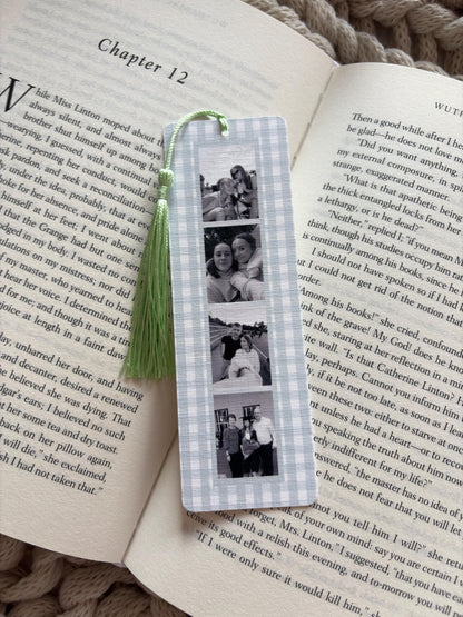 A rectangular bookmark with a light blue and white gingham pattern featuring four vertical black and white photographs of people. A light green tassel is attached to the top of the bookmark with a small loop, resting on an open book.