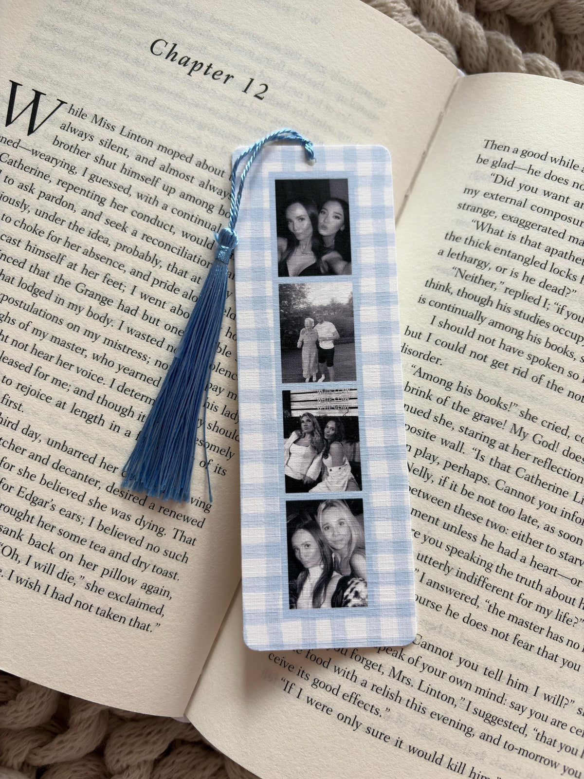 A rectangular bookmark with a light blue and white gingham pattern, featuring four vertical black and white photographs of people. A light blue silk tassel is attached to the top with a matching blue string, resting on an open book.