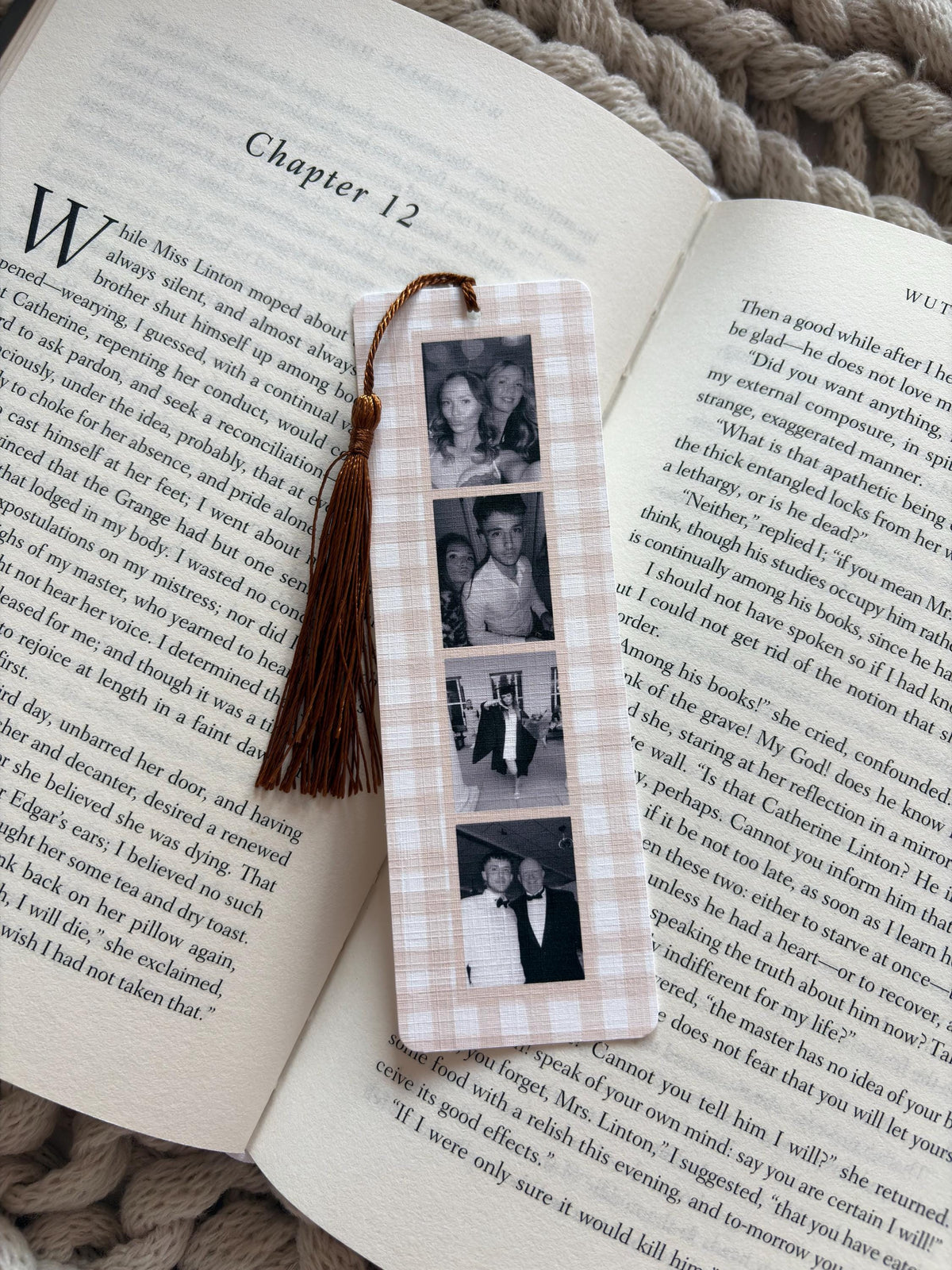 A rectangular bookmark with a light beige and white gingham pattern featuring four vertical black and white photographs. A dark brown tassel is attached to the top center of the bookmark, which is resting on an open book page.