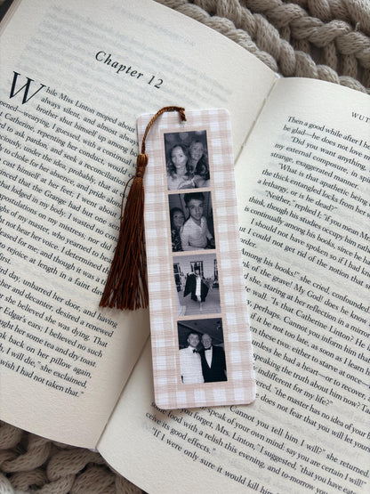 A rectangular bookmark with a light beige and white gingham pattern featuring four vertical black and white photographs. A dark brown tassel is attached to the top center of the bookmark, which is resting on an open book page.