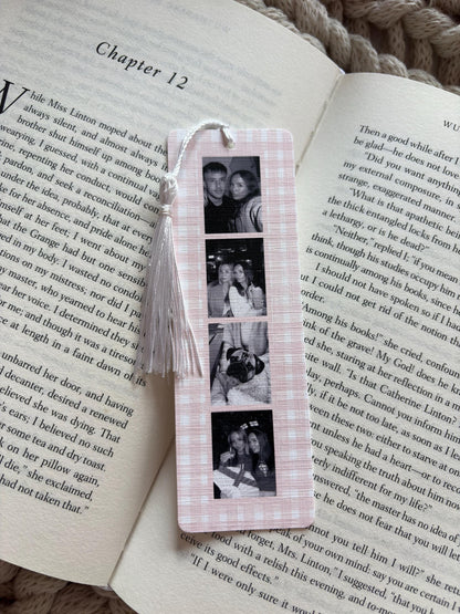 A rectangular bookmark with a light pink and white gingham pattern featuring four vertical black and white photographs of people and a dog. A white tassel is attached to the top of the bookmark, which is resting on an open book.