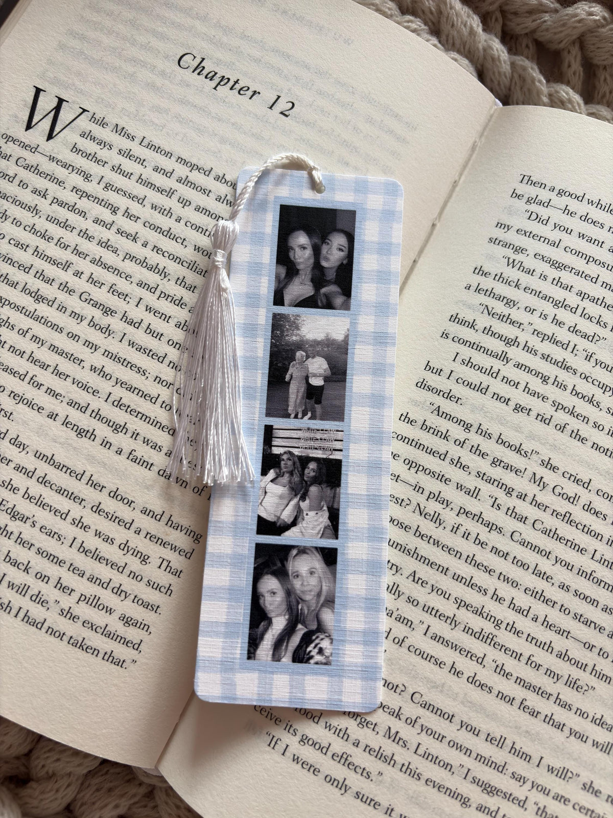 A rectangular bookmark with a light blue and white gingham pattern featuring four vertical black and white photographs of people. A white tassel is attached to the top center hole of the bookmark, which is resting on an open book page.