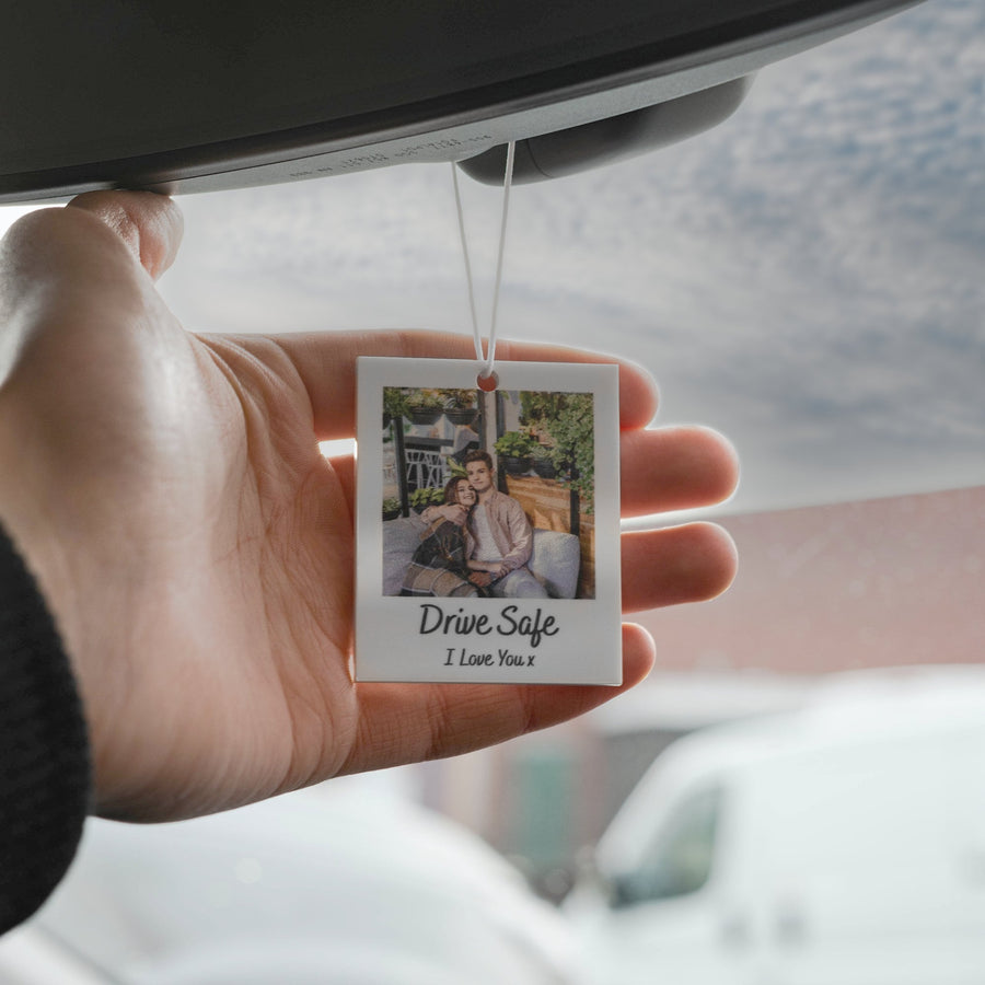 White car air freshener with a photo of a couple in a Polaroid frame. The text "Drive Safe I Love You x" is printed below the photo.