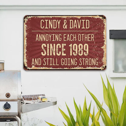 A rectangular, distressed metal sign with a burgundy background and cream-colored text. The sign reads "CINDY & DAVID ANNOYING EACH OTHER SINCE 1989 AND STILL GOING STRONG."