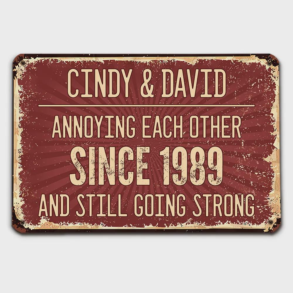 A rectangular, distressed metal sign with a burgundy background and cream-colored text. The sign reads "CINDY & DAVID ANNOYING EACH OTHER SINCE 1989 AND STILL GOING STRONG."