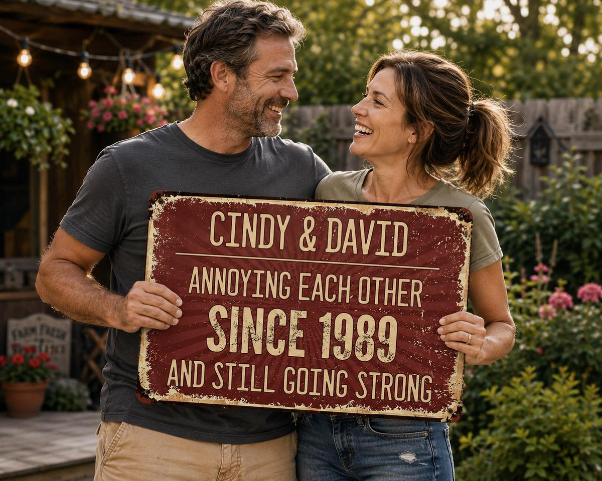A distressed burgundy metal sign with the text "Cindy & David Annoying Each Other Since 1989 And Still Going Strong." The sign is held by a smiling couple in front of a garden.