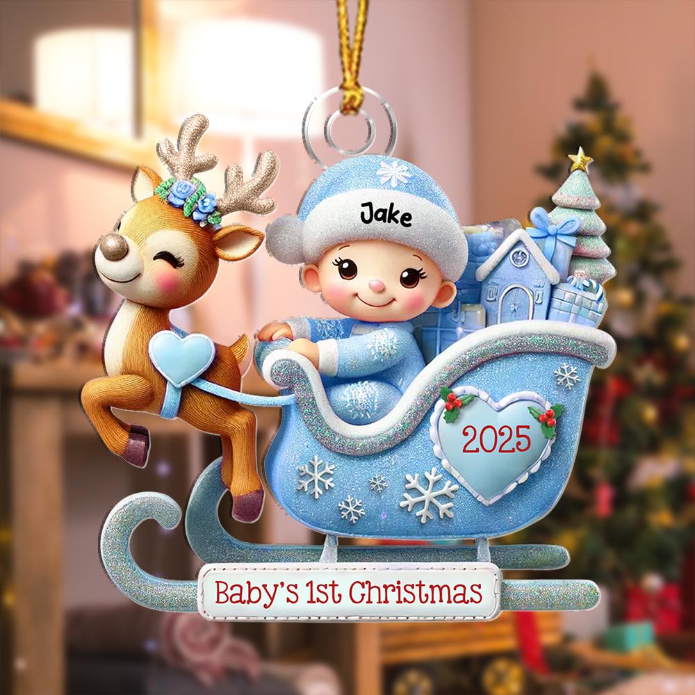 May include: A Christmas ornament featuring a reindeer pulling a light blue glittery sleigh with a baby wearing a blue hat labeled Jake. The sleigh displays the year 2025 on a heart and a banner at the bottom with the text Baby's 1st Christmas.
