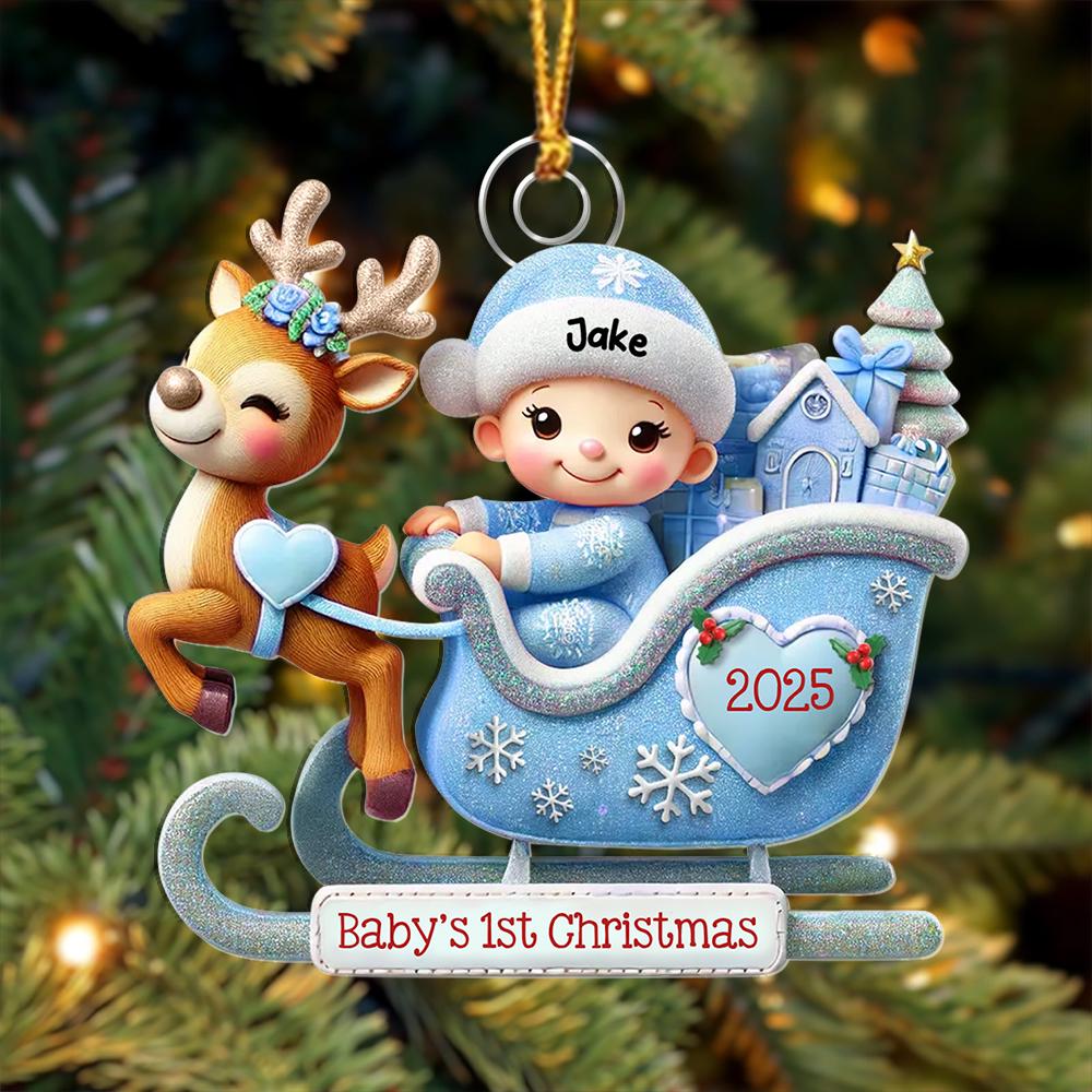 May include: A Christmas ornament featuring a brown reindeer with a blue floral crown pulling a light blue glittery sleigh. A baby in a blue hat labeled Jake sits inside with gifts and a tree. A heart on the sleigh says 2025, and a sign reads Baby's 1st Christmas.