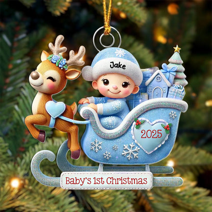 May include: A Christmas ornament featuring a brown reindeer with a blue floral crown pulling a light blue glittery sleigh. A baby in a blue hat labeled Jake sits inside with gifts and a tree. A heart on the sleigh says 2025, and a sign reads Baby's 1st Christmas.