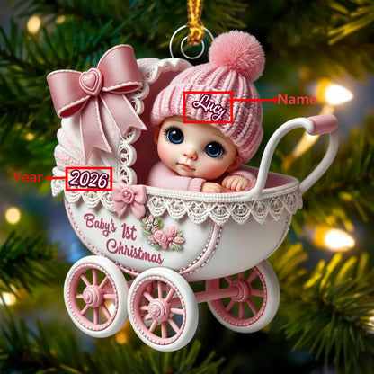 May include: A decorative Christmas ornament shaped like a white and pink baby carriage with a baby wearing a pink knit hat. The carriage features a large pink bow, lace trim, and the text Baby's 1st Christmas, 2026, and a placeholder for a name.