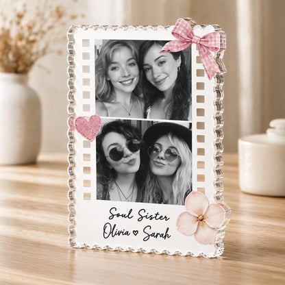 May include: A clear acrylic photo frame with a scalloped edge, featuring two black and white photographs of two pairs of women. The frame is decorated with a pink gingham bow, a pink glitter heart, and a pink flower, with the text Soul Sister Olivia Sarah.