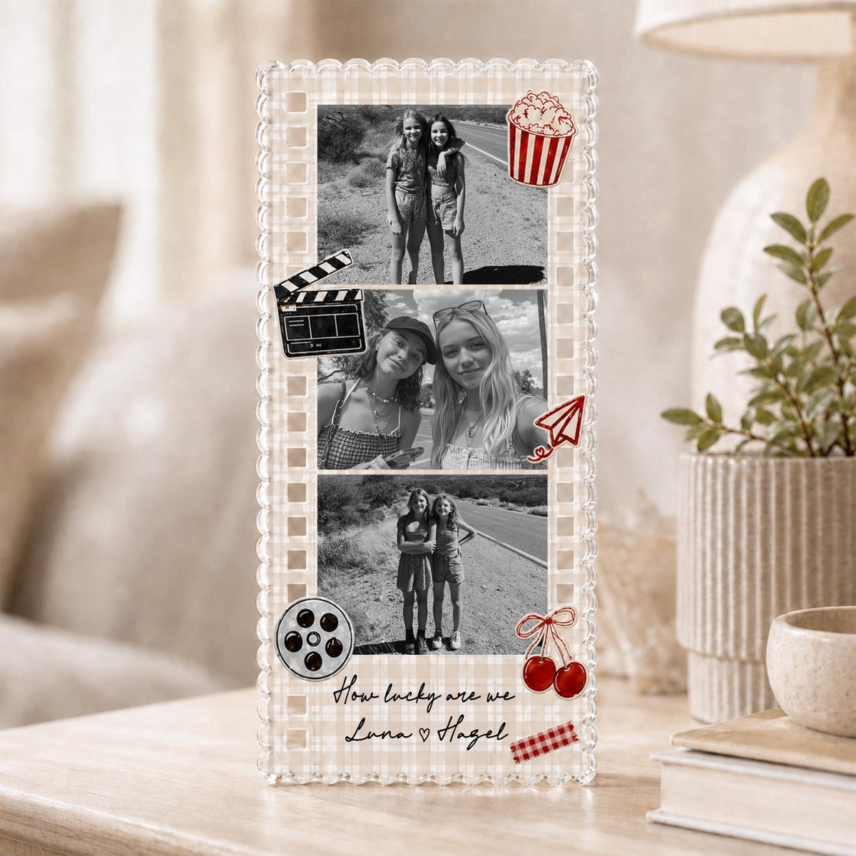 May include: A rectangular acrylic photo frame with a beige gingham border featuring three black and white photographs of two people. Decorative red icons include a popcorn bucket, film clapper, paper plane, and cherries. Text reads: How lucky are we Luna ♡ Hagel.