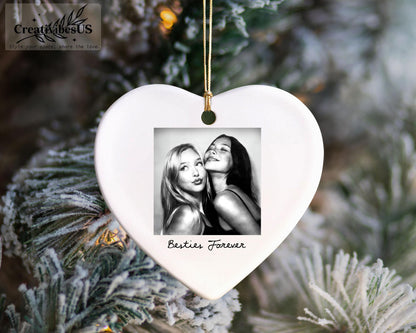 A white heart-shaped ceramic ornament featuring a square black and white photograph of two people posing together. The text "Besties Forever" is printed in black script below the photo. A gold string is attached for hanging.