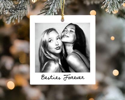 A square white ceramic ornament shaped like a vintage instant photo frame. The center features a black and white photograph of two people posing together. Below the photo, the text Besties Forever is printed in a black cursive font.