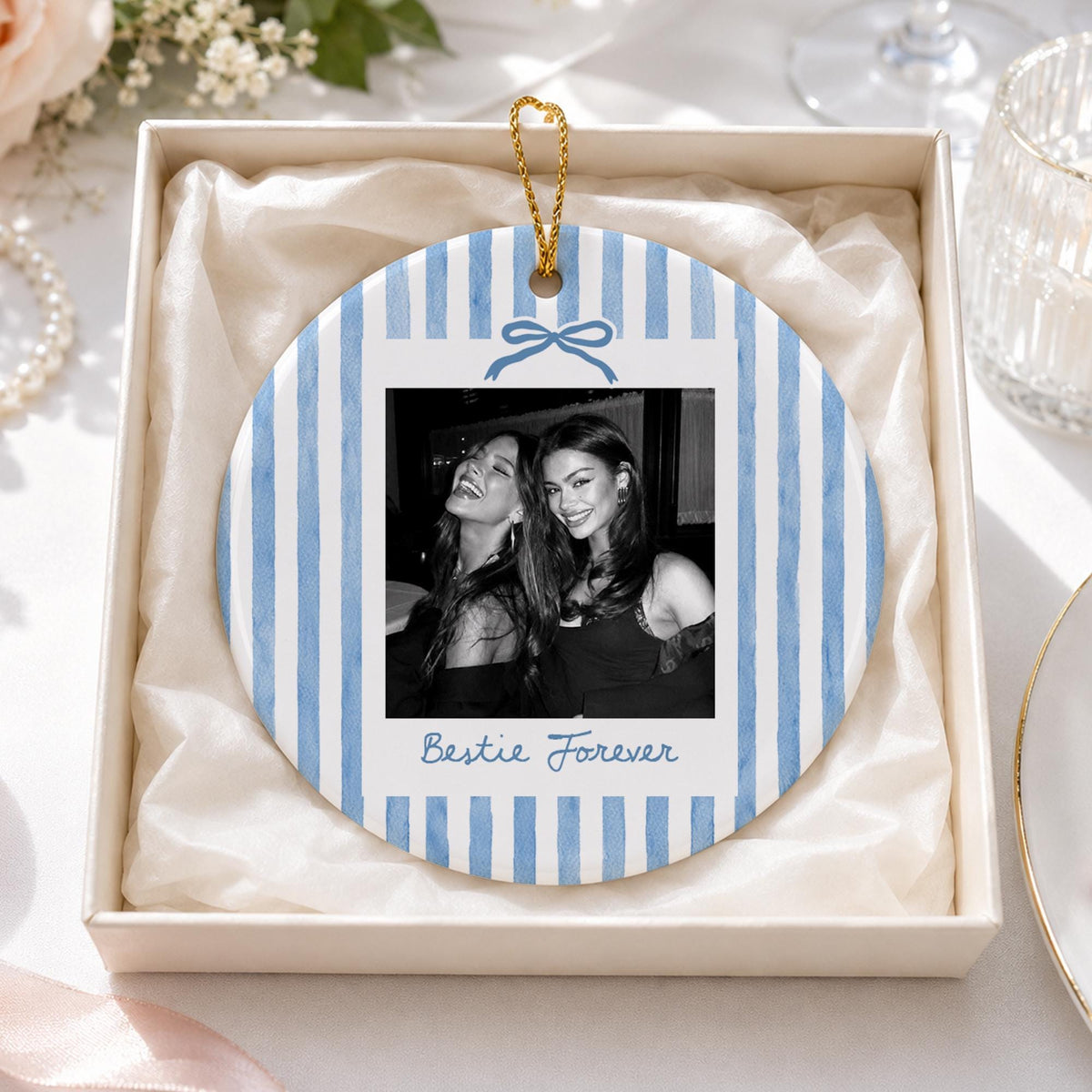 A round ceramic ornament featuring a light blue and white vertical striped pattern. The center displays a black and white photograph of two people, topped with a blue bow graphic and the text Bestie Forever in blue script.