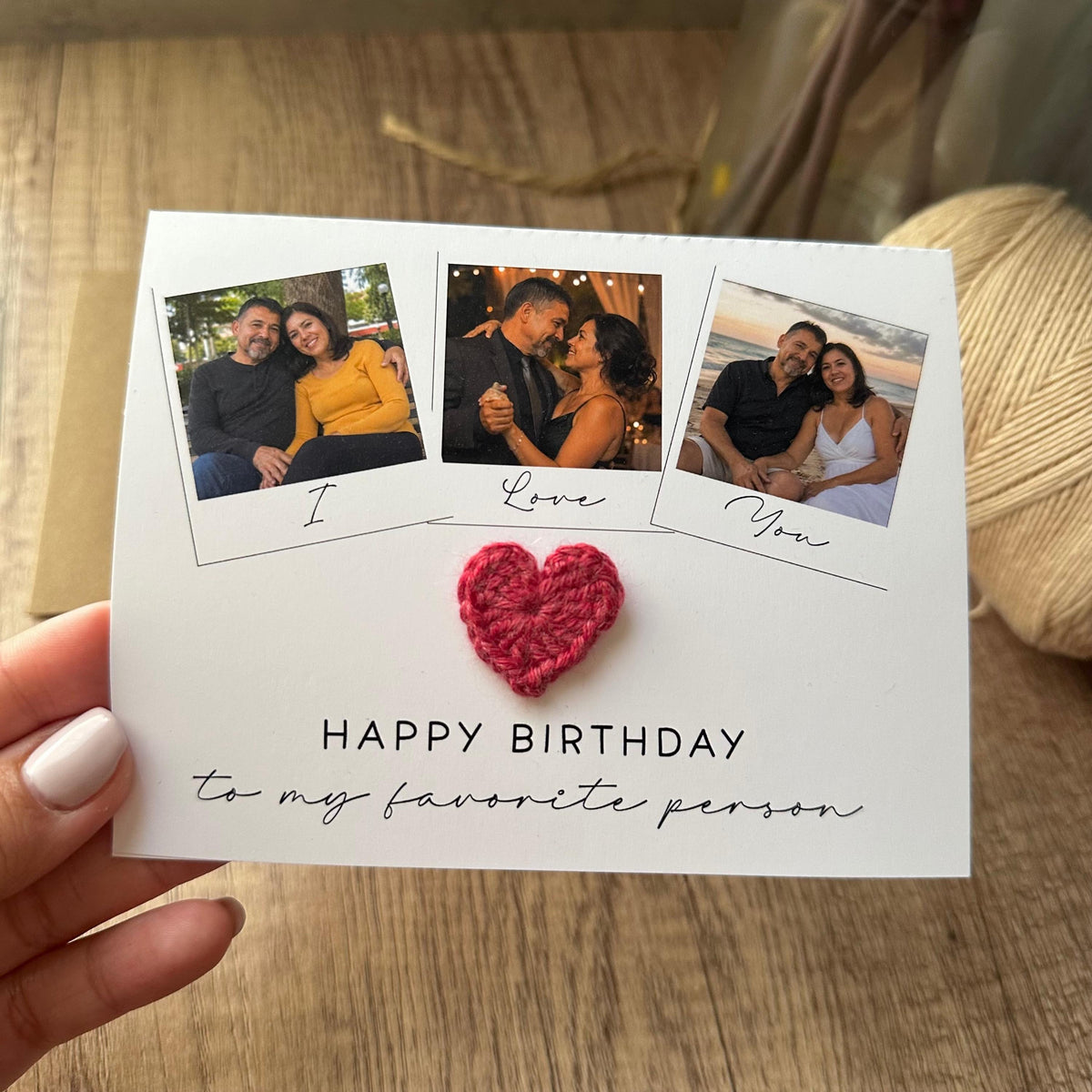 A white greeting card featuring three square photo frames with the text I Love You underneath them. A small red crocheted heart is attached to the center. The text HAPPY BIRTHDAY to my favorite person is printed below the heart.