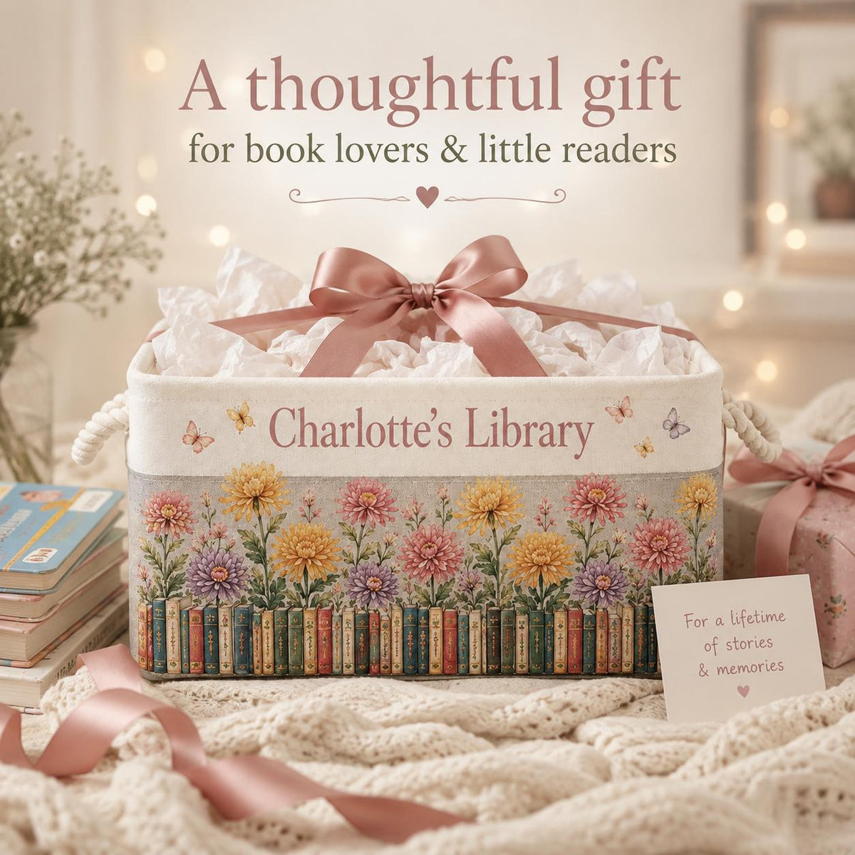 May include: A rectangular fabric storage bin with a pink satin bow, featuring the text "Charlotte's Library" and a printed design of colorful chrysanthemums above a row of books. Small butterflies are scattered across the cream-colored surface.