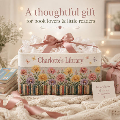 May include: A rectangular fabric storage bin with a pink satin bow, featuring the text "Charlotte's Library" and a printed design of colorful chrysanthemums above a row of books. Small butterflies are scattered across the cream-colored surface.