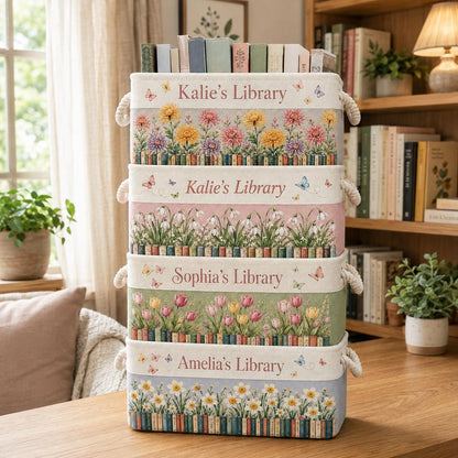 May include: A stack of four rectangular fabric storage bins with rope handles. Each bin features a floral print, a row of book spines, and custom text: Kalie's Library, Kalie's Library, Sophia's Library, and Amelia's Library, with butterflies throughout.