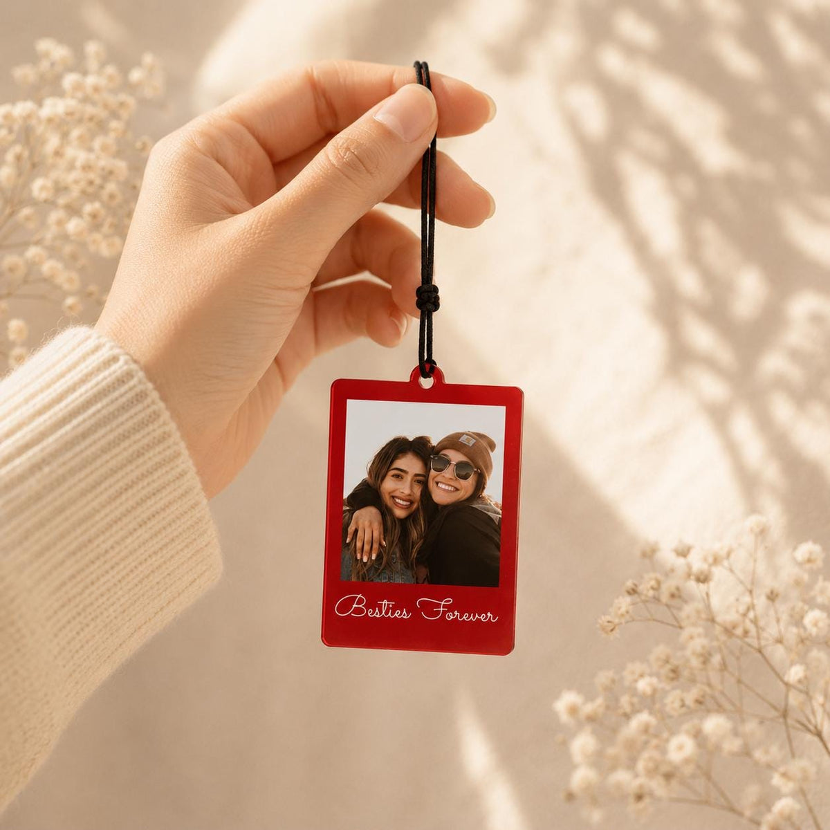 A rectangular red acrylic photo ornament featuring a printed image of two people smiling together. The text Besties Forever is printed in white cursive script at the bottom. The ornament hangs from a thin black cord with a knot.