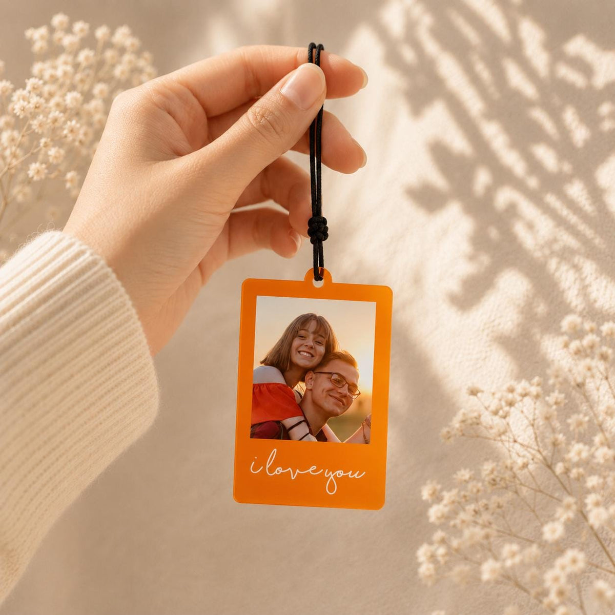 A rectangular orange photo ornament featuring a printed image of a couple embracing. The bottom of the orange frame displays the white cursive text "i love you". The ornament hangs from a thin black cord with a small knot detail.