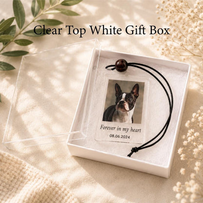 A white gift box with a clear lid containing a rectangular acrylic ornament. The ornament features a photograph of a black and white dog, the text "Forever in my heart," and the date "08.06.2024," attached to a black cord.