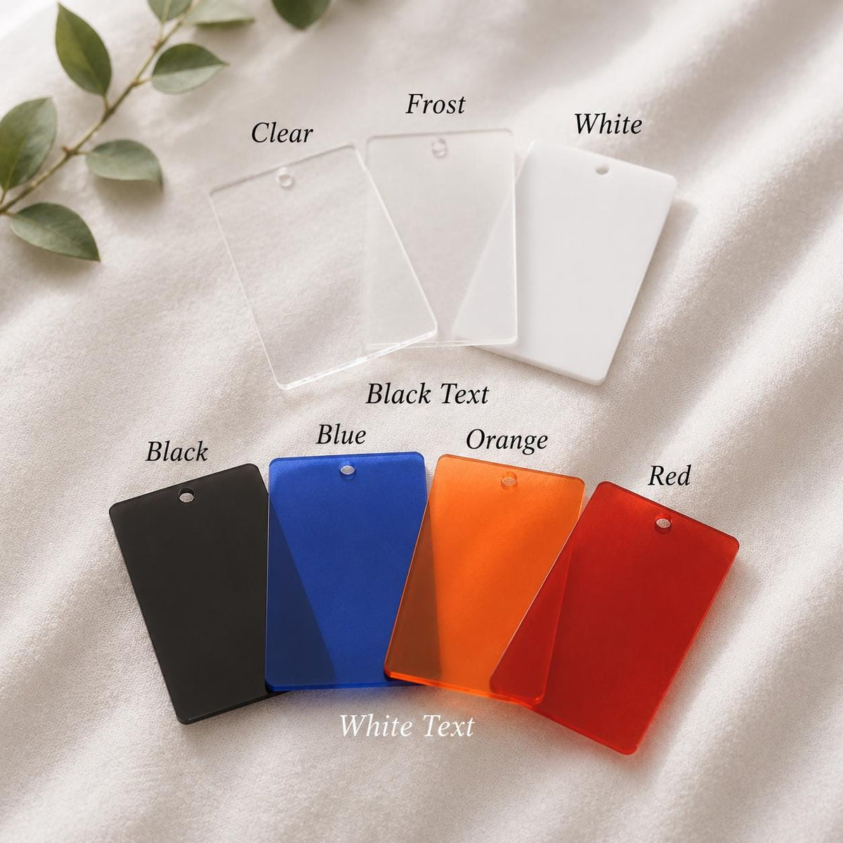 A collection of seven rectangular acrylic tags with pre-drilled holes at the top. The top row includes clear, frost, and white tags. The bottom row features black, blue, orange, and red tags. Labels indicate Black Text and White Text.