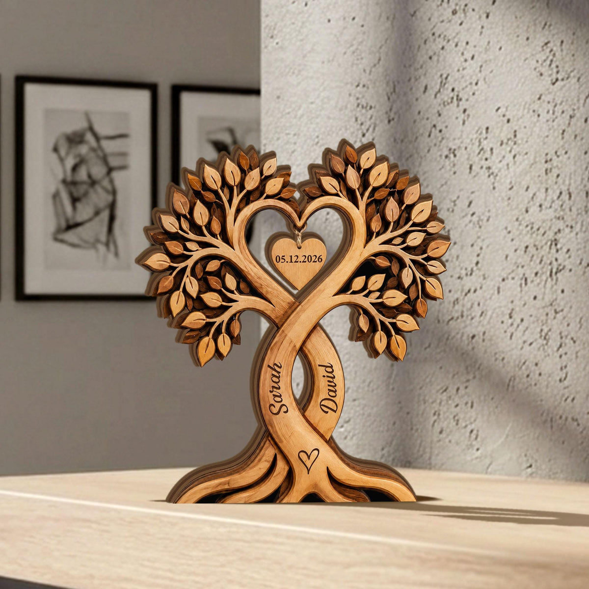 May include: A wooden tree sculpture with intertwined trunks, forming a heart shape at the top. The sculpture features engraved names "Sarah" and "David", a heart symbol, and the date "05.12.2026". The tree has detailed leaf carvings and a natural wood finish.