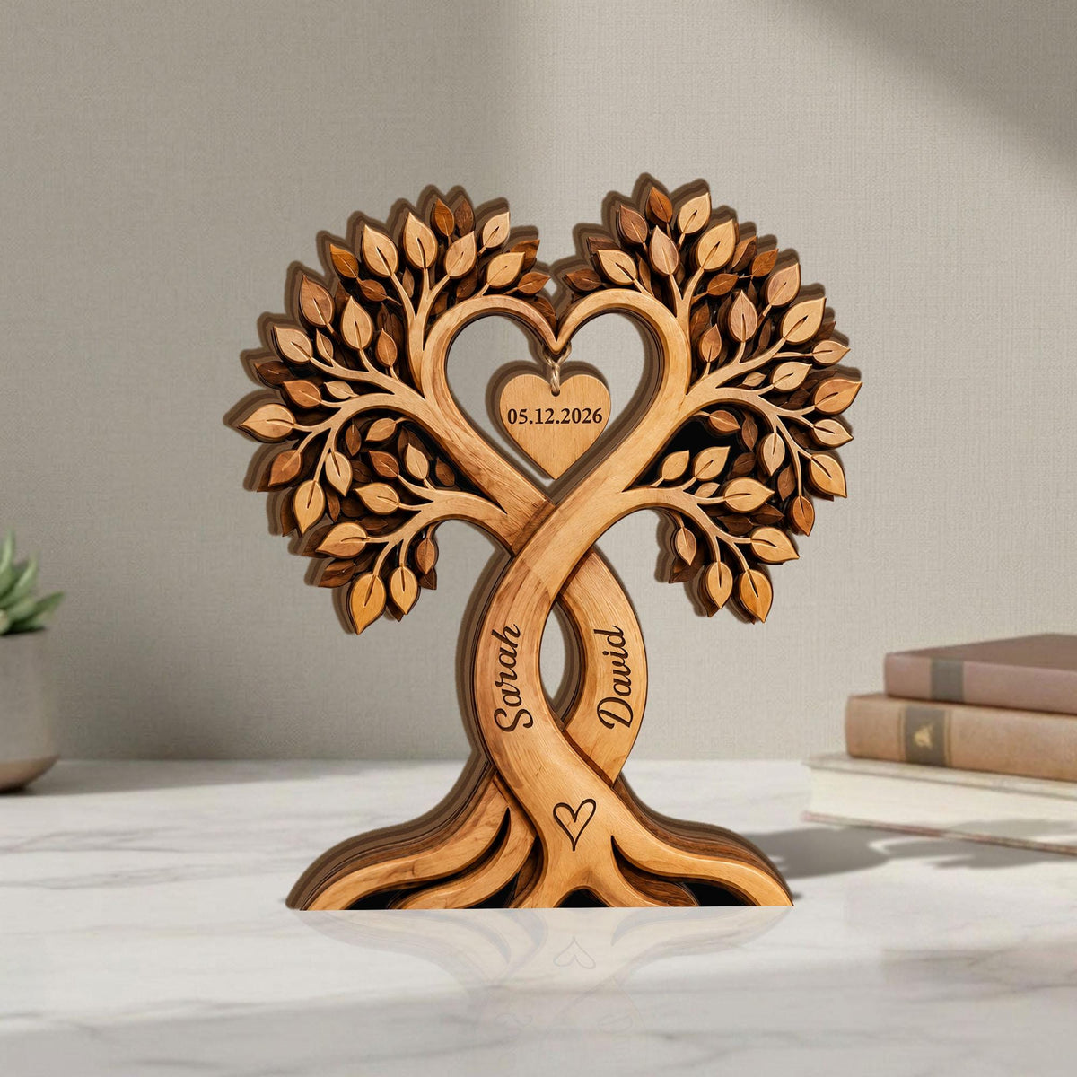 May include: A wooden tree sculpture with intertwined trunks, forming a heart shape. The sculpture features the names "Sarah" and "David" and a heart-shaped tag with the date "05.12.2026". The tree has detailed leaf carvings and a small heart at the base.