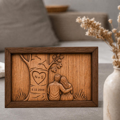 May include: A wooden plaque with a carved design. The design features a tree with a heart-shaped carving containing the initials "N+S" and the date "6.12.2008". Two figures are embracing under the tree. The plaque is framed in a dark brown wood.