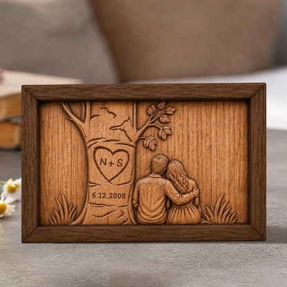 May include: A wooden plaque with a carved design. The design features a tree with a heart-shaped carving containing the initials "N+S" and the date "6.12.2008". Below the tree, a couple is depicted embracing. The plaque is framed in dark brown wood.
