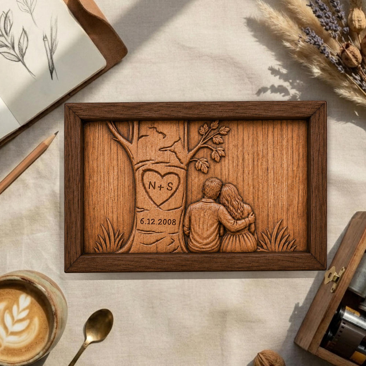 May include: A wooden framed carving featuring a couple embracing under a tree. The tree has a heart with the initials "N+S" and the date "6.12.2008" carved into it. The frame is dark brown.