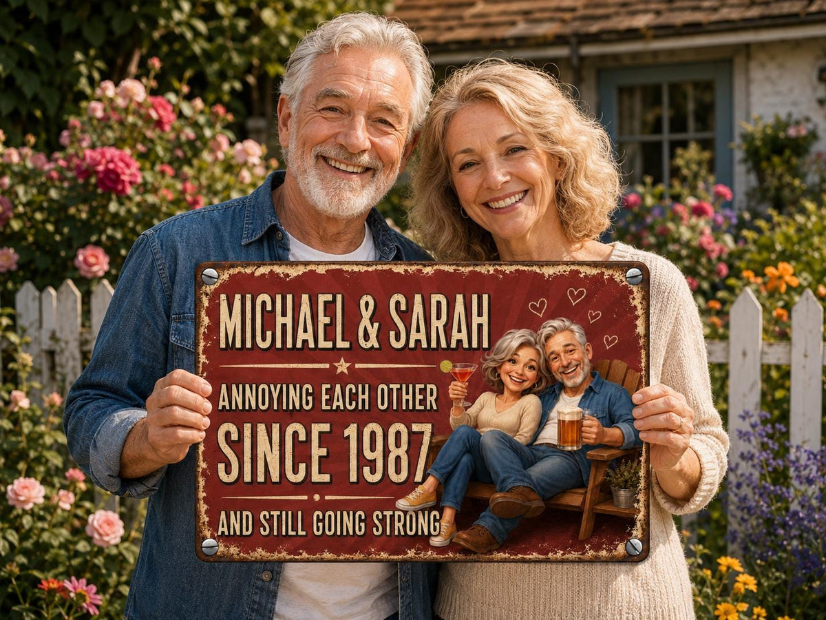 A rectangular metal sign with a distressed red background featuring the text "MICHAEL & SARAH ANNOYING EACH OTHER SINCE 1987 AND STILL GOING STRONG". The sign displays a cartoon illustration of a couple sitting on a wooden bench.