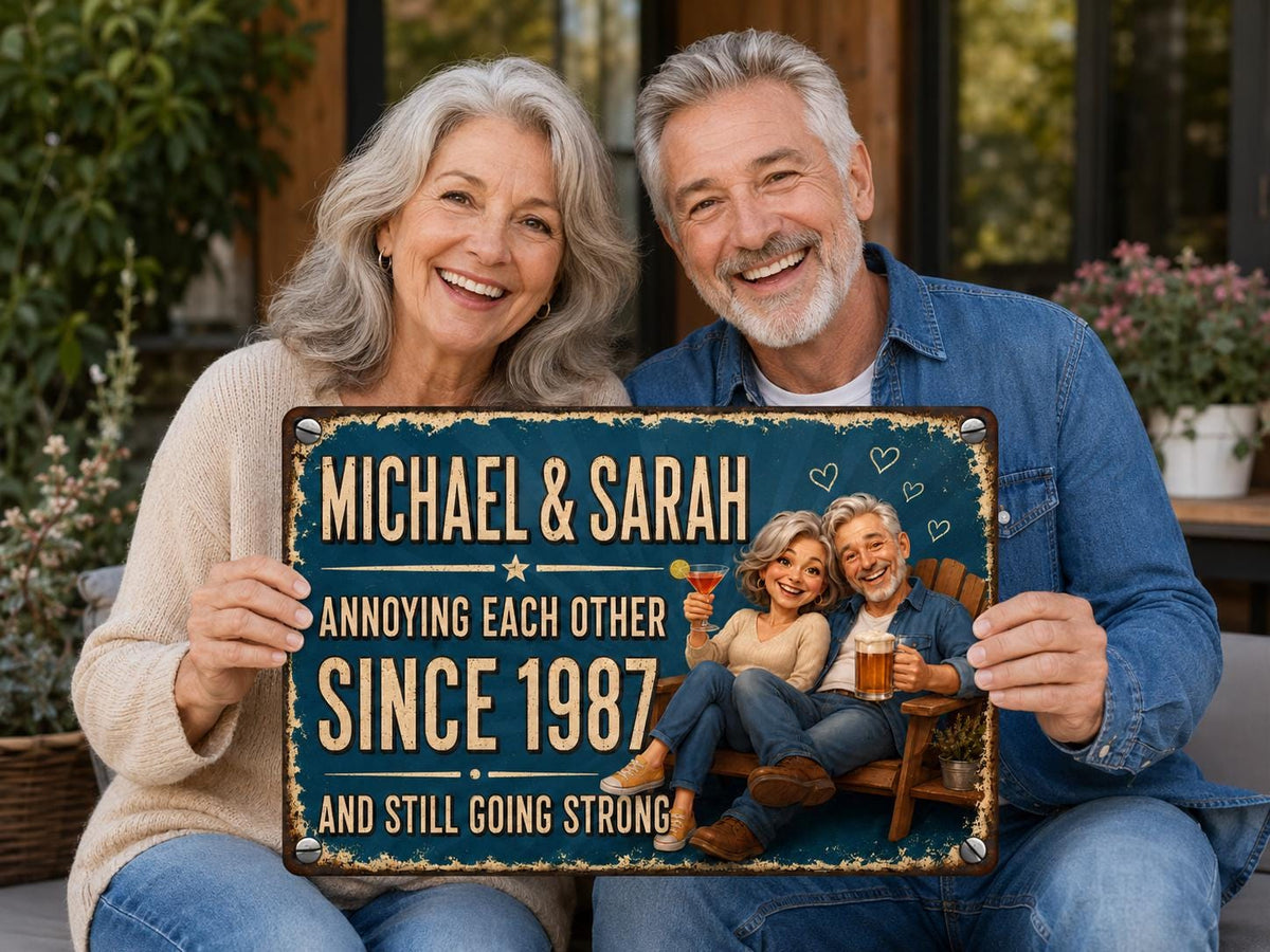 A rectangular metal sign with a dark blue distressed background featuring the text MICHAEL & SARAH ANNOYING EACH OTHER SINCE 1987 AND STILL GOING STRONG. The sign displays a cartoon illustration of a couple sitting in a wooden chair.