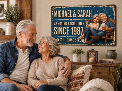 A rectangular metal wall sign with a blue background featuring the text MICHAEL & SARAH ANNOYING EACH OTHER SINCE 1987 AND STILL GOING STRONG. The sign displays a cartoon illustration of a couple sitting in a wooden chair.