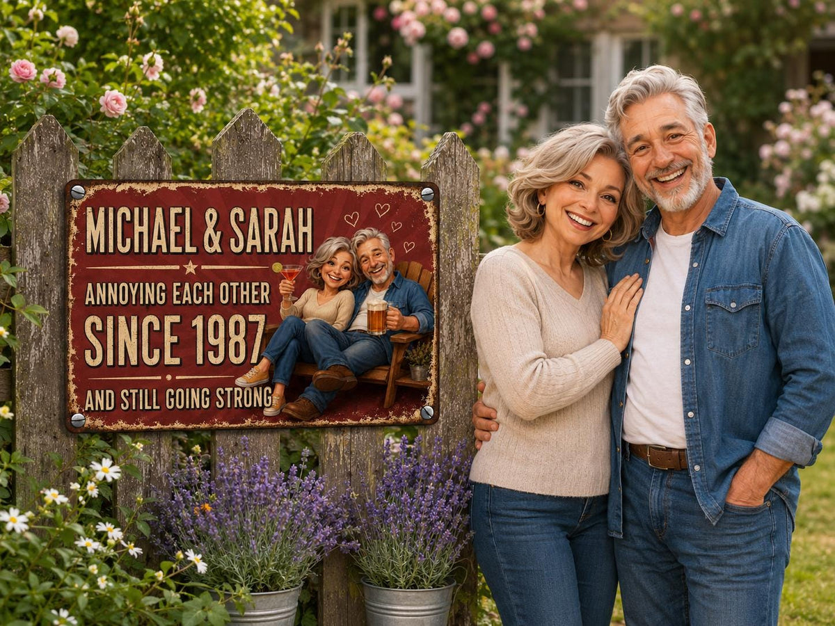 A rectangular metal sign with a distressed red finish featuring the text MICHAEL & SARAH ANNOYING EACH OTHER SINCE 1987 AND STILL GOING STRONG. The sign displays a cartoon illustration of a couple sitting on a wooden bench.