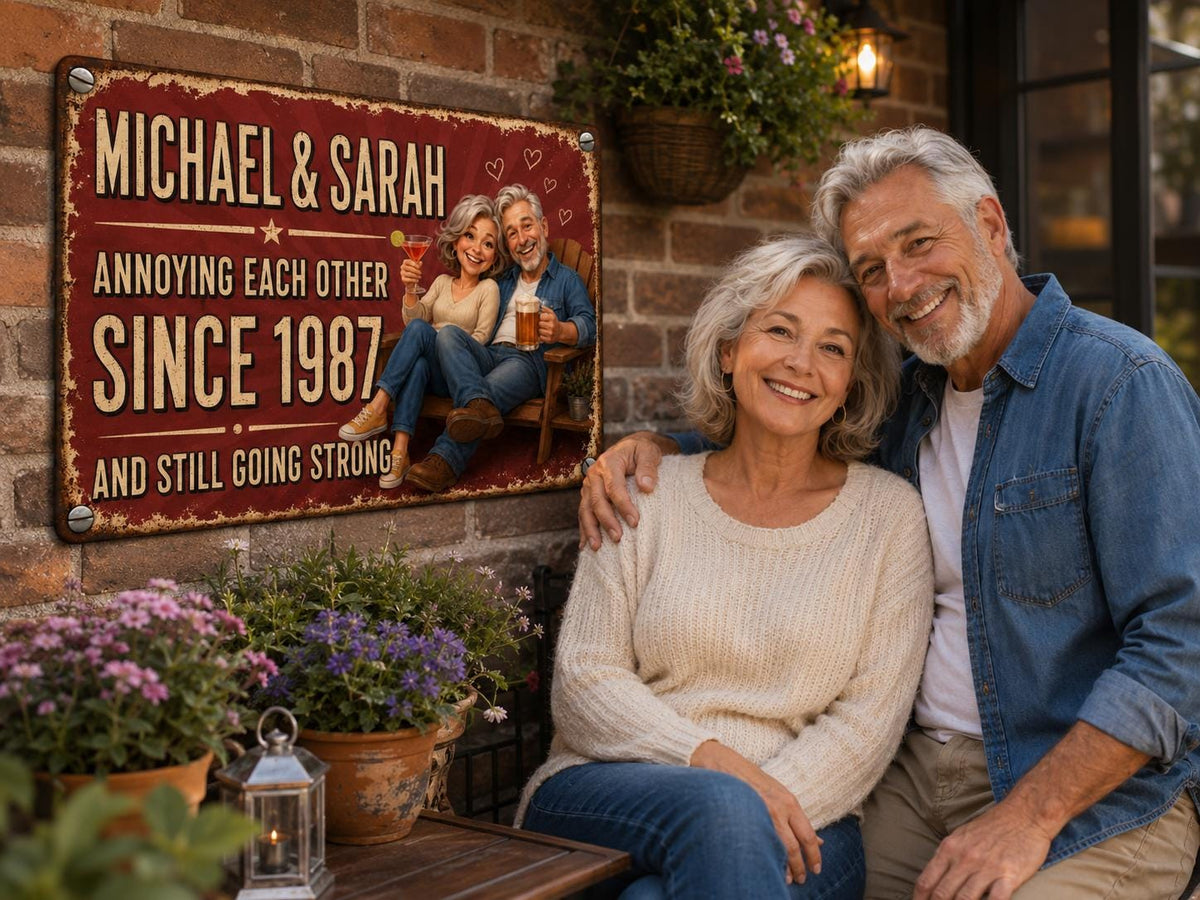 A rectangular metal sign with a distressed red background featuring the text MICHAEL & SARAH ANNOYING EACH OTHER SINCE 1987 AND STILL GOING STRONG. The sign displays a cartoon illustration of a couple sitting on a wooden bench.