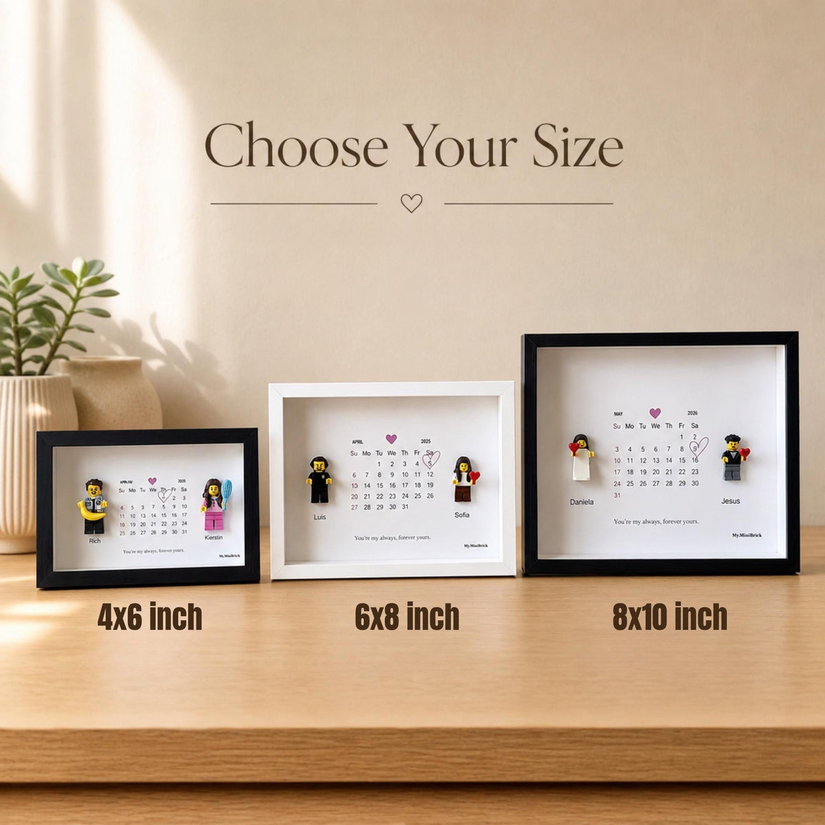 Three shadow box frames in 4x6 inch, 6x8 inch, and 8x10 inch sizes, each containing a calendar print with a heart icon, personalized names, and two small plastic toy figures. The text Choose Your Size is displayed above the frames.