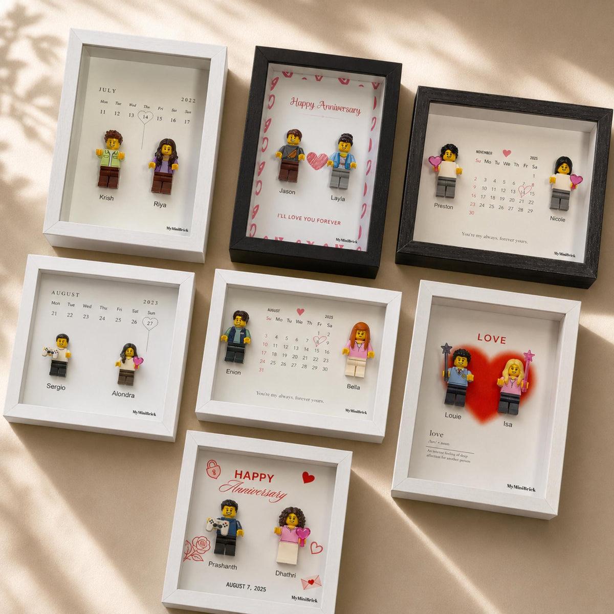 Seven shadow box frames containing personalized calendar prints and two plastic minifigures. Each frame features a unique date, names, and decorative elements like hearts or stars. The frames are white or black with glass fronts.
