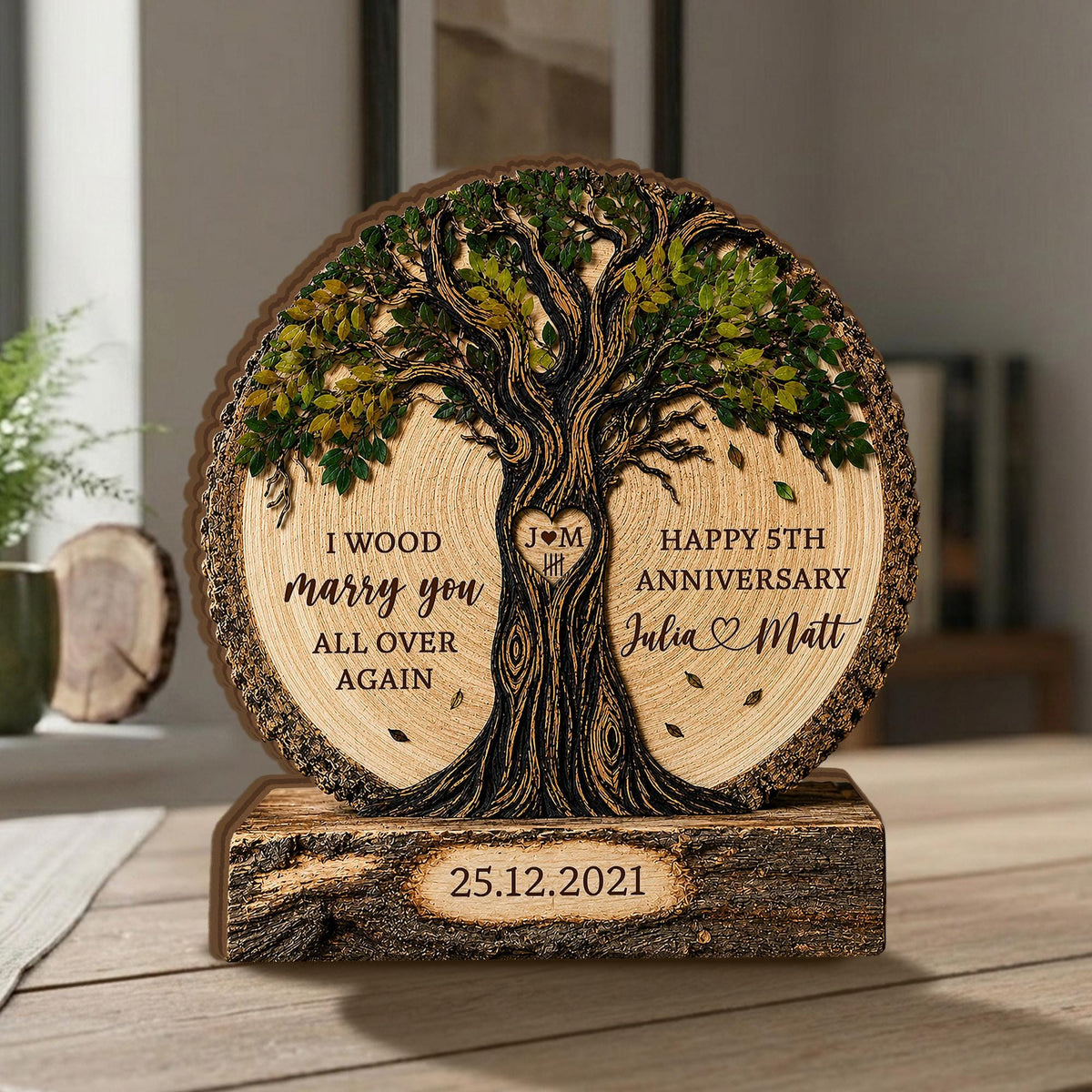 May include: A circular wooden plaque featuring a carved tree with green leaves, resting on a rectangular log base. The plaque displays the text "I WOOD marry you ALL OVER AGAIN", "HAPPY 5TH ANNIVERSARY", "Julia & Matt", and the date "25.12.2021".