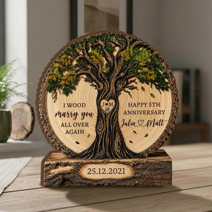 May include: A circular wooden plaque featuring a carved tree with green leaves, resting on a rectangular log base. The plaque displays the text "I WOOD marry you ALL OVER AGAIN", "HAPPY 5TH ANNIVERSARY", "Julia & Matt", and the date "25.12.2021".
