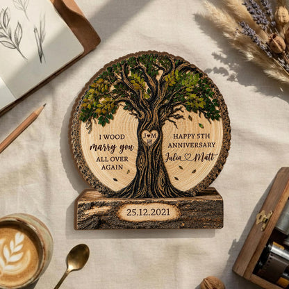 May include: A circular wooden plaque featuring a laser-engraved tree with green foliage. The text reads I WOOD marry you ALL OVER AGAIN, HAPPY 5TH ANNIVERSARY, Julia and Matt, and the date 25.12.2021. A heart with J M is carved in the trunk.