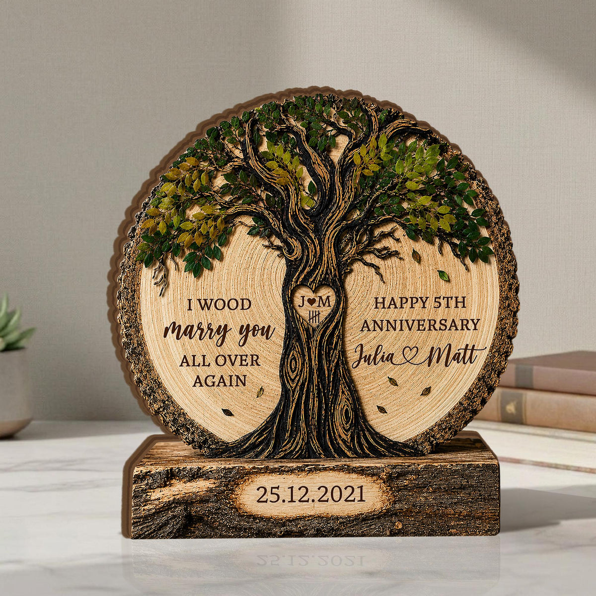 May include: A circular wooden plaque featuring a carved tree with green leaves. The text reads: I WOOD marry you ALL OVER AGAIN, HAPPY 5TH ANNIVERSARY, Julia and Matt, and 25.12.2021. A heart with J M and tally marks is on the tree trunk.